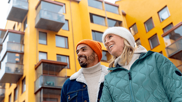 pariskunta seisoo kerrostalon edessä ja hymyilee