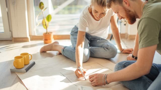 mies ja nainen istuvat lattialla ikkunan edessä ja suunnittelevat taloa